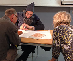 Two museum visitors sit at a table watching a Babylonian diviner read their future from a tray of oil and water